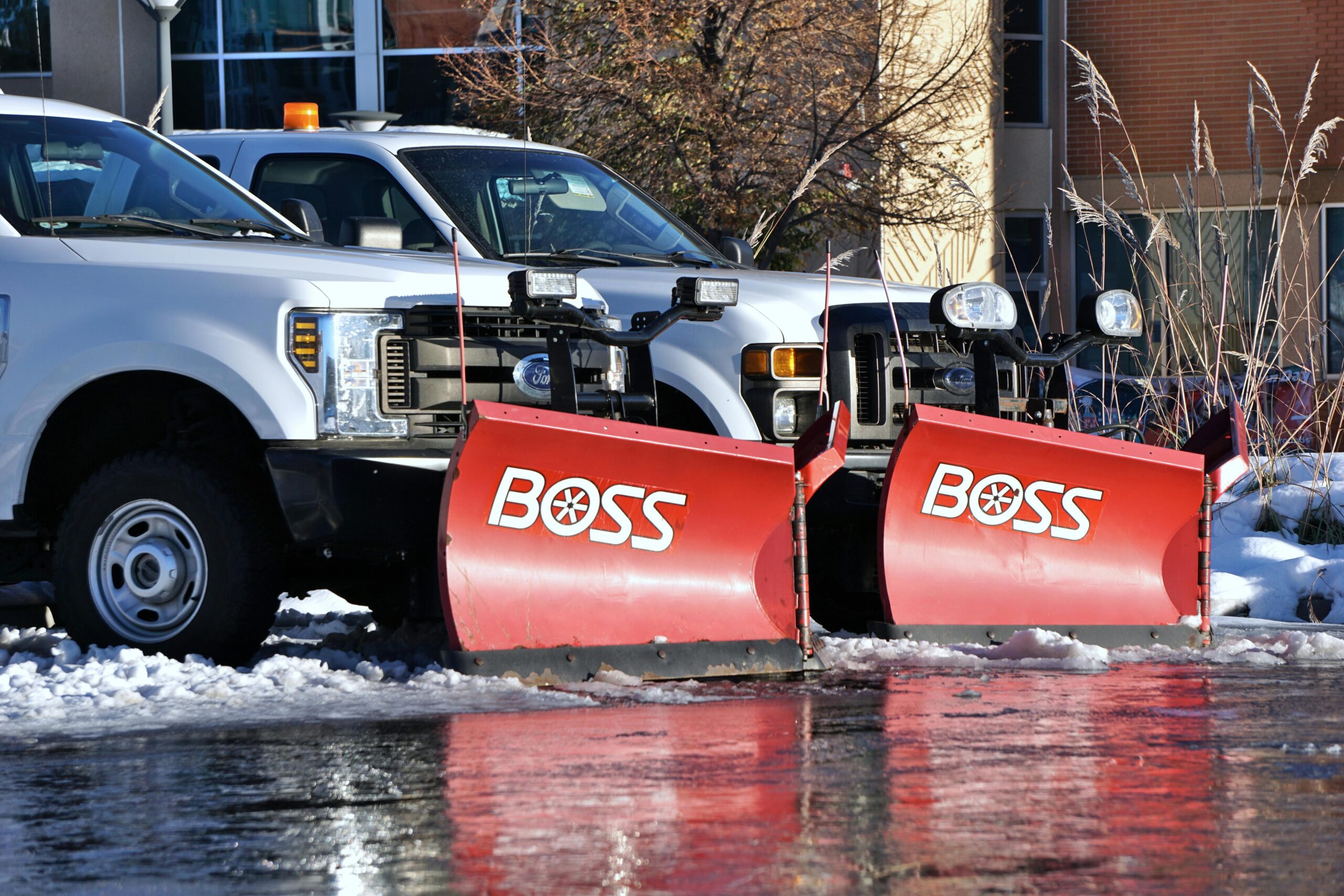 White pickup trucks with red snow plows, poised for winter road clearing.